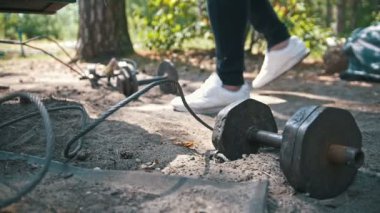 Atlet gelir ve ağır demir dumbbell ormandaki kumdan yükseltir
