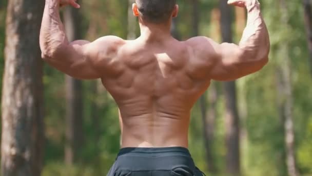 Homem muscular posando musculação na floresta de verão - bíceps enorme — Vídeo de Stock