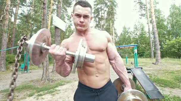 Büyük kas silah damarları ile genç adam ormanda ağır dumbbells alır — Stok video