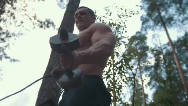 Gespierde jongeman die zich bezighouden met zware ijzeren halters in het bos — Stockvideo