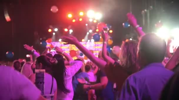 Multitud de personas bailando levantando las manos en un concierto - globos multicolores volando alrededor de la sala de conciertos — Vídeos de Stock