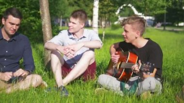 Arkadaşlar güneş altında çimlerde oturan bulutlar bakıyor