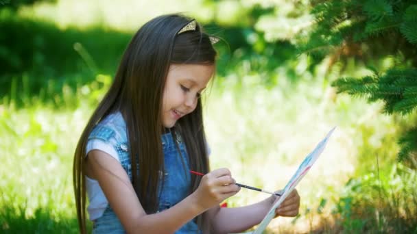 Happy little girl drawing watercolor paints sitting on the grass at sunny day — Stock Video