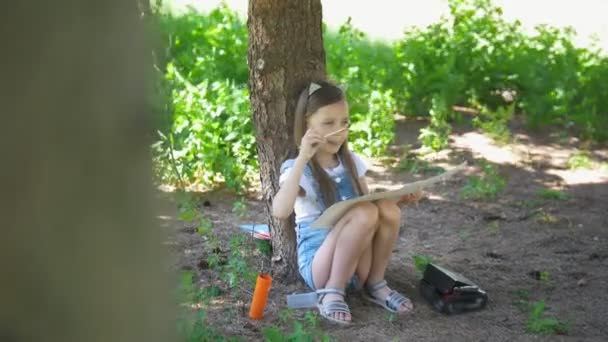 Kaukasische meisje tekenen met borstel zittend onder de boom op de zomer — Stockvideo