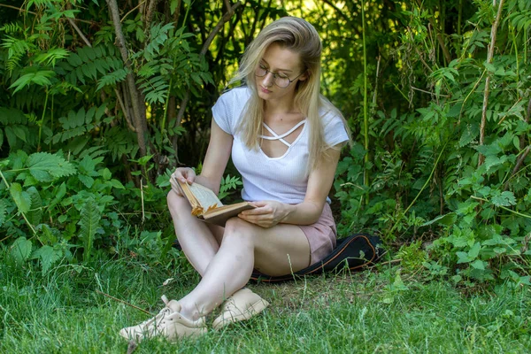 Молодая привлекательная женщина читает книгу под деревом в парке в солнечный день — стоковое фото