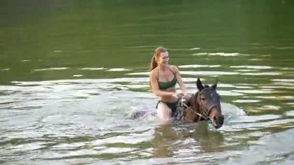 Две счастливые женщины едут на лошади по реке в воде — стоковое видео