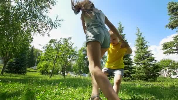 Милый маленький мальчик убегает от своей счастливой сестры через елки в солнечный день — стоковое видео