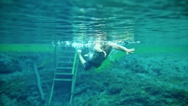 Gespierde man onderwater zwemmen in de helderblauwe lake — Stockvideo