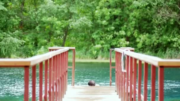 Young man gets out of the lake on the pier — Stock Video