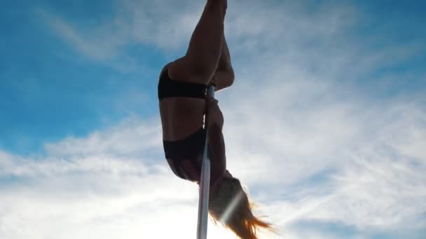 Young sexy woman doing exercises on the pylon against the blue sky outdoors — Stock Video