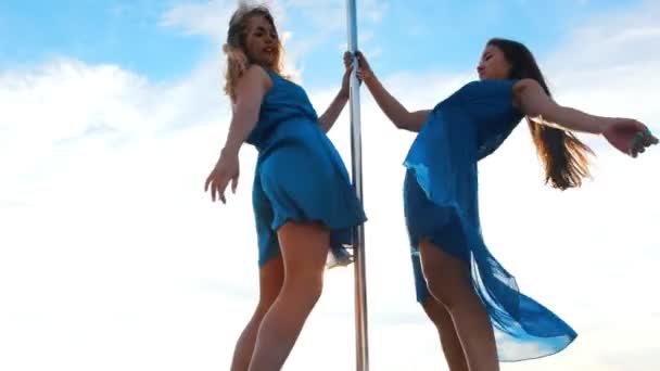 İki genç kadın dansçı mavi elbiseler gerçekleştirir mavi gökyüzüne karşı bir pole-dans — Stok video