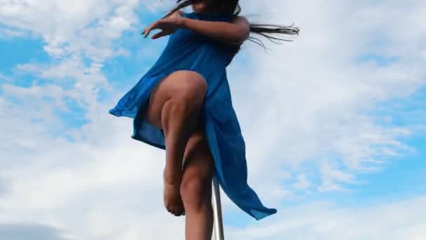 Приваблива жінка в блакитній сукні, що виконує полюс-танцювання на небі — стокове відео