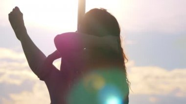 Genç kadın direk dansör gün batımına karşı direğe asılı