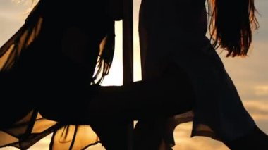 Genç kadın siluetleri günbatımında pole-dans gerçekleştirir