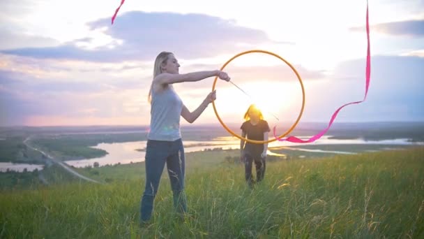 Young female acrobats exercising on the hill - girl jumps through the hoop at sunset outdoors — Stock Video
