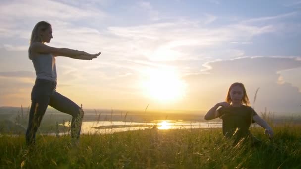 Dos mujeres jóvenes calentándose en la colina al atardecer de verano — Vídeos de Stock