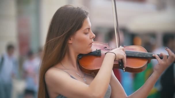 Молодая кавказская женщина играет на скрипке на пешеходной улице в летний день — стоковое видео