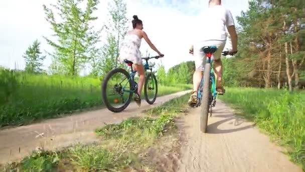 Молодая счастливая пара катается на велосипеде по тропе в летнем поле — стоковое видео