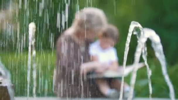 Kleiner Junge und Großmutter lesen Buch im Park — Stockvideo