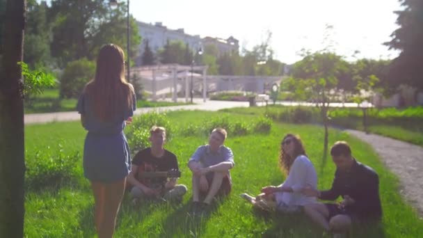 Mujer joven muestra pantomima delante de amigos sentados en el césped en el parque de verano — Vídeo de stock