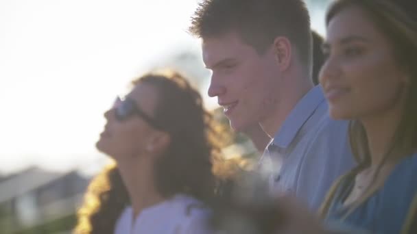 Jóvenes amigos caucásicos divirtiéndose y cantando canciones con una guitarra en el parque de verano al atardecer — Vídeos de Stock