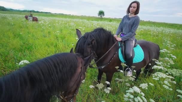 El caballo comiendo hierba delante de jinete hembra a caballo en el campo — Vídeos de Stock