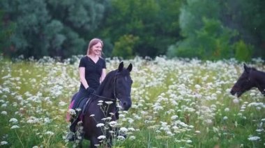 Mutlu genç kadınlar çiçeklerle alanında siyah at sırtında binmek