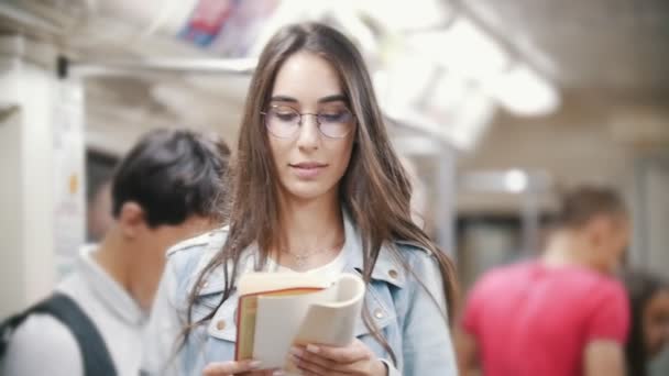 Flicka läsa en bok på tunnelbanan och ser tillbaka på personer — Stockvideo