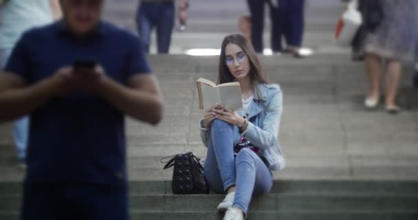 젊은 여성이 지하철에서 계단에 앉아서 책을 읽고 — 비디오