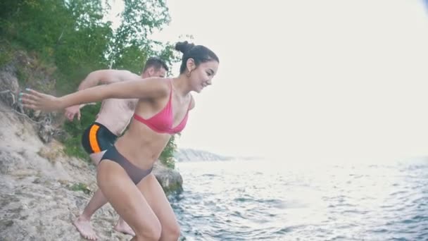 Flicka med en kille som hoppa tillsammans i vattnet på en semester i naturen, slow motion — Stockvideo