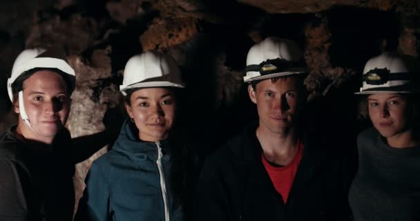 Jóvenes amigos exploradores mirando a la cámara en una cueva oscura — Vídeo de stock