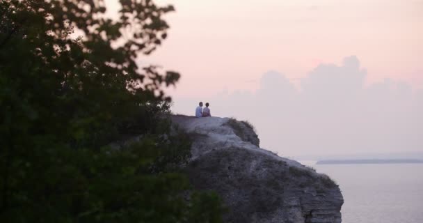 Jeune homme et femme assis sur une montagne profitant du coucher du soleil — Video