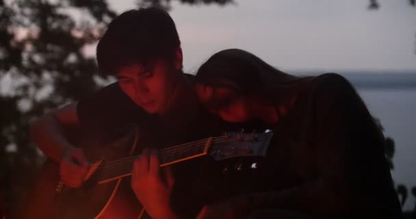 Giovane coppia godendo la ricreazione - uomo che suona la chitarra e vicino al falò di notte — Video Stock