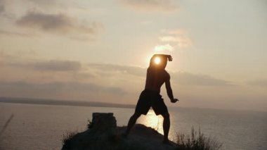 Genç adam bir bir uçurumun üstünde güneş doğarken ısınma