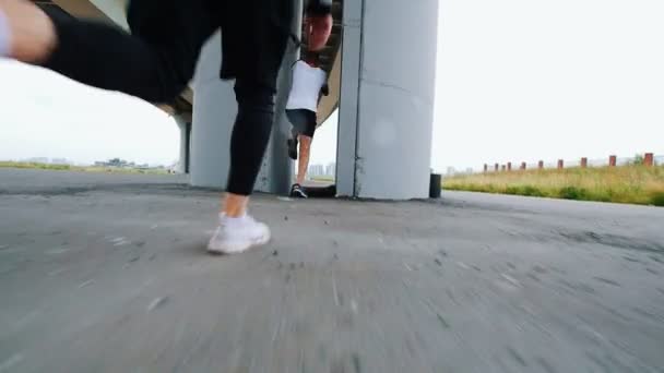 Під мостом біжать двоє хлопців, роблячи стрибки — стокове відео