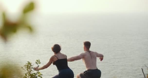 Молодой человек и женщина делают утреннюю разминку на скалистом утесе у реки — стоковое видео