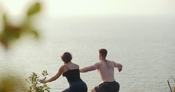 Joven hombre y mujer haciendo el calentamiento matutino en el acantilado rocoso junto al río — Vídeos de Stock