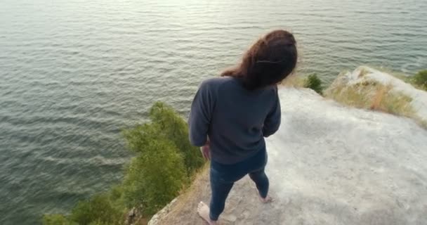 Vista trasera de una mujer joven calentándose en el borde de un acantilado al amanecer — Vídeos de Stock