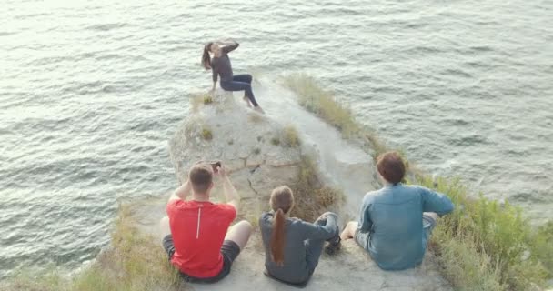 Young friends sitting on the mountain shooting a beautiful woman on the edge of a cliff — Stock Video