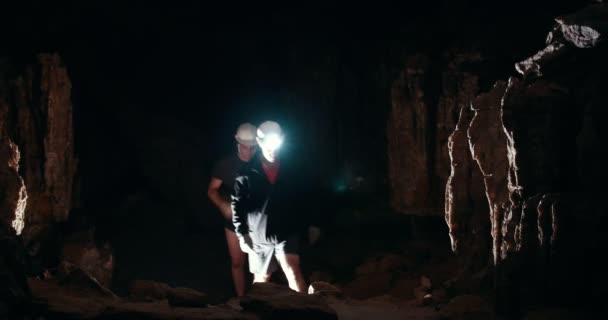 Due giovani speleologi con torcia camminano in una grotta buia — Video Stock