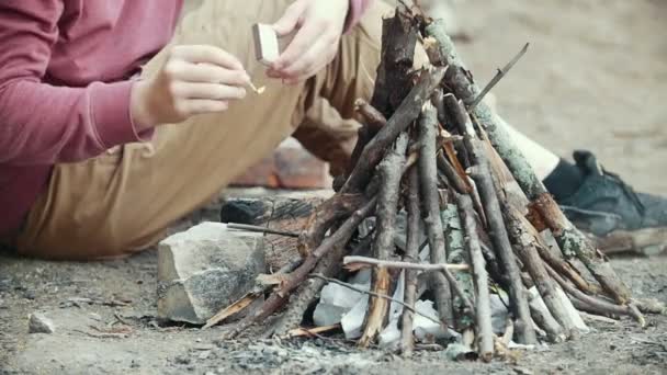 Men hand with a match lights a branches into small bonfire in the forest — Stock Video