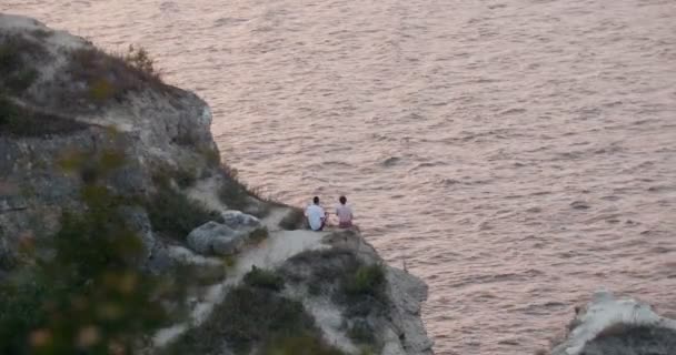 Jong koppel zit op rotsachtige klif aan zee — Stockvideo