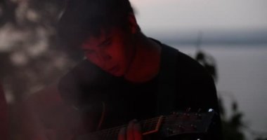 Genç adam ormandaki şenlik ateşi tarafından gitar çalmak