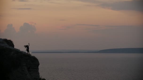 Weibliche Silhouette wirft ihre langen Haare in den Wind am Rande der Klippe bei Sonnenuntergang — Stockvideo