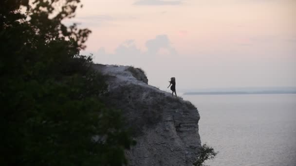 Молода жінка танцює на скелі під морем — стокове відео