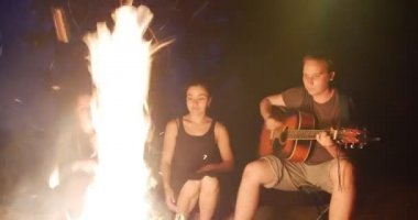 Şarkı gitar ve iki kız ormanda kamp ateşi tarafından oturan genç adam