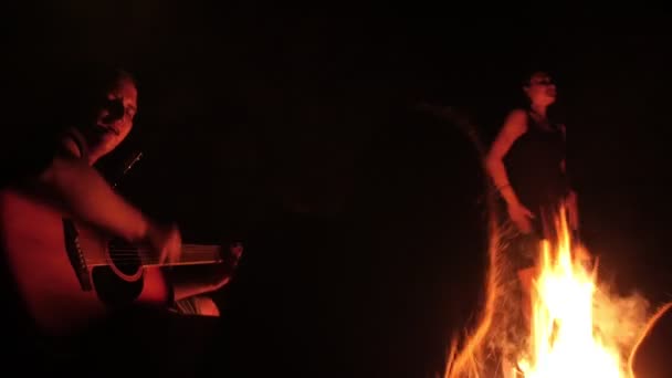 Jonge vrienden een gitaar spelen, meisje dansen door de bonfire's nachts — Stockvideo