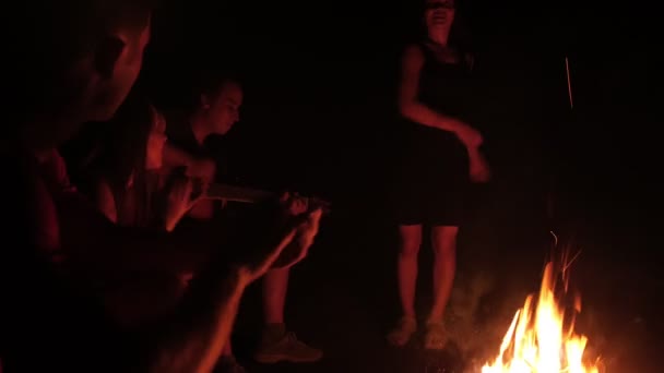 Mujer joven bailando delante de sus amigos cantando y aplaudiendo junto a la hoguera por la noche — Vídeo de stock