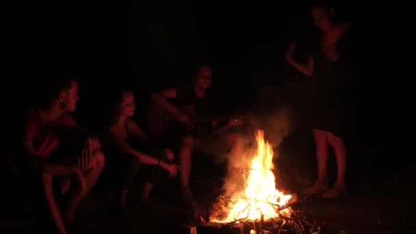 Atractiva mujer bailando junto a la fogata y sus amigas cantando y aplaudiendo por la noche — Vídeo de stock