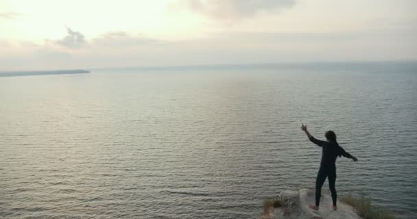 Giovane donna che fa ginnastica mattutina sul bordo di una scogliera vicino al mare — Video Stock